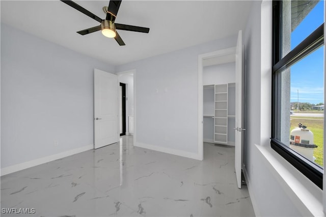 unfurnished bedroom featuring baseboards, a spacious closet, marble finish floors, and a ceiling fan