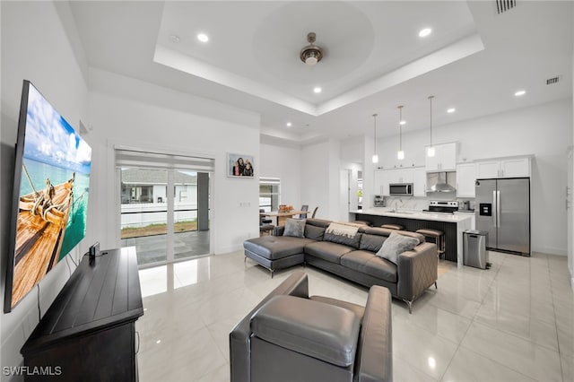 living area with a high ceiling, a raised ceiling, a ceiling fan, recessed lighting, and baseboards