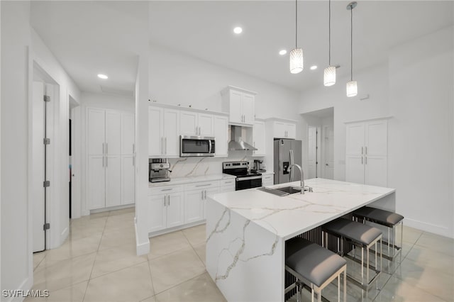 kitchen with stainless steel appliances, wall chimney range hood, a kitchen island with sink, white cabinetry, and recessed lighting