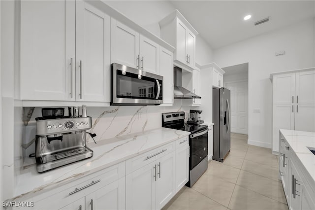 kitchen with appliances with stainless steel finishes, wall chimney range hood, white cabinetry, light stone countertops, and baseboards