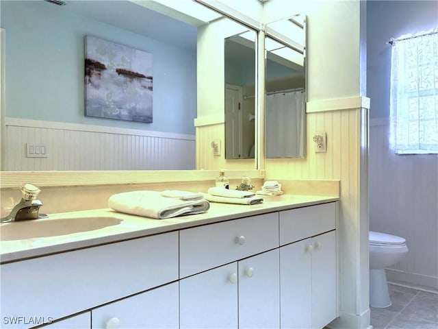 full bath with a wainscoted wall, toilet, vanity, and tile patterned flooring