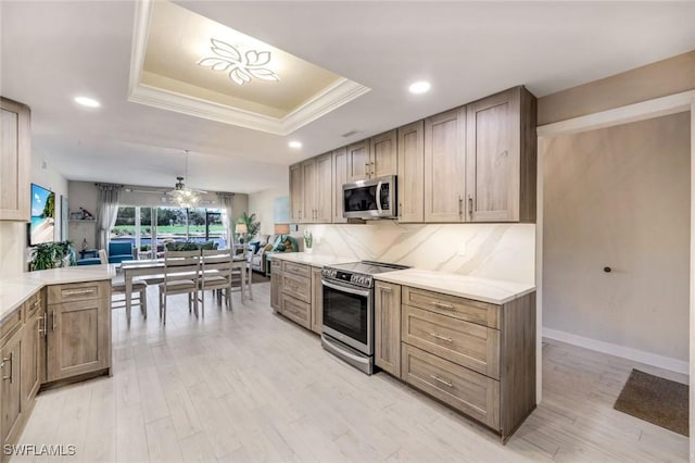 kitchen with appliances with stainless steel finishes, a tray ceiling, light wood-style flooring, recessed lighting, and light countertops
