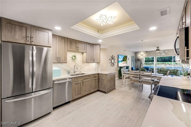 kitchen with stainless steel appliances, a raised ceiling, a sink, light countertops, and crown molding
