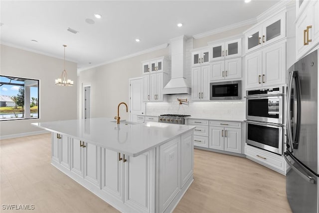 kitchen with appliances with stainless steel finishes, a sink, wall chimney exhaust hood, tasteful backsplash, and light countertops
