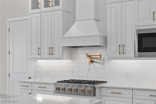 kitchen with custom exhaust hood, appliances with stainless steel finishes, white cabinetry, light countertops, and glass insert cabinets