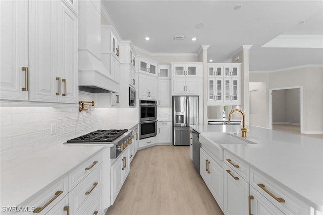 kitchen featuring appliances with stainless steel finishes, white cabinets, premium range hood, a sink, and recessed lighting