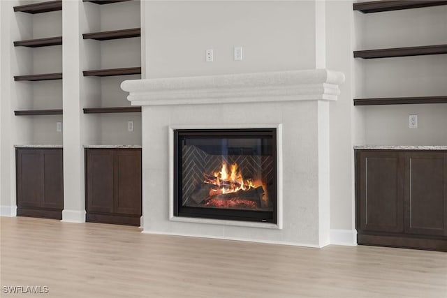 detailed view of wood finished floors, a glass covered fireplace, baseboards, and built in features