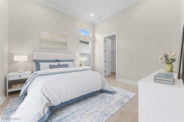 bedroom featuring ornamental molding, light wood finished floors, baseboards, and a walk in closet