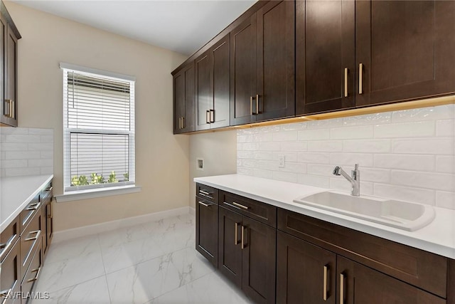 kitchen with a sink, baseboards, light countertops, dark brown cabinets, and light marble finish flooring