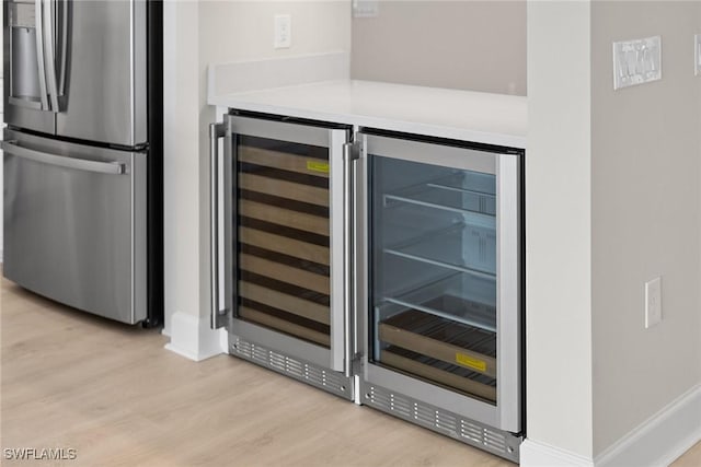 kitchen view of stainless steel refrigerator with ice dispenser, light wood finished floors, a bar, wine cooler, and baseboards