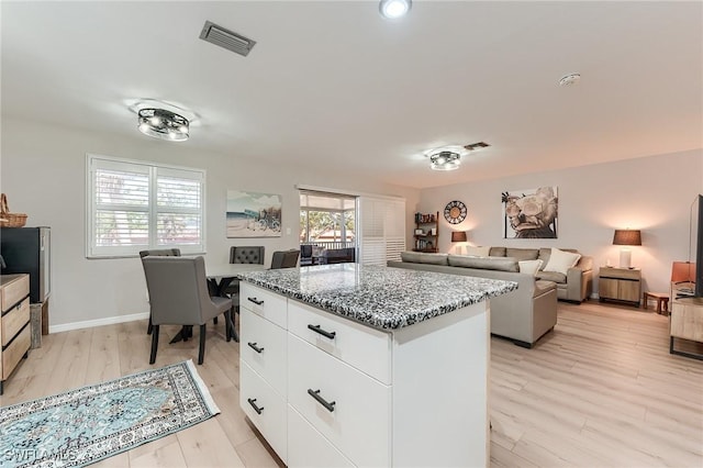 114 Lovers Ln, Fort Myers Beach, FL 33931 - kitchen with a center island, light stone counters, white cabinetry, light wood-type flooring, and baseboards