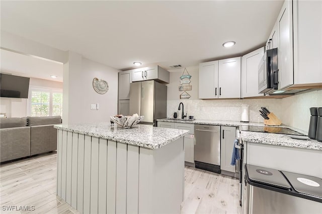 114 Lovers Ln, Fort Myers Beach, FL 33931 - kitchen featuring appliances with stainless steel finishes, a sink, light wood finished floors, a kitchen island, and light stone countertops