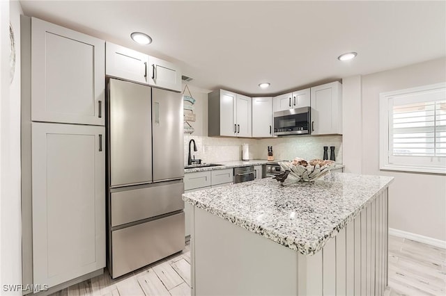 114 Lovers Ln, Fort Myers Beach, FL 33931 - kitchen featuring appliances with stainless steel finishes, a sink, light stone countertops, tasteful backsplash, and a center island