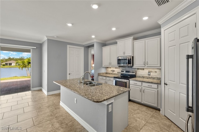 kitchen with stainless steel appliances, a sink, tasteful backsplash, an island with sink, and baseboards