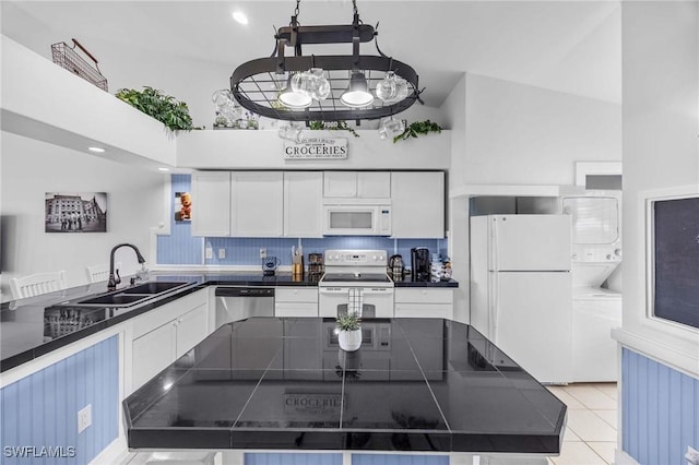 kitchen with white appliances, stacked washing machine and dryer, a sink, dark countertops, and a towering ceiling