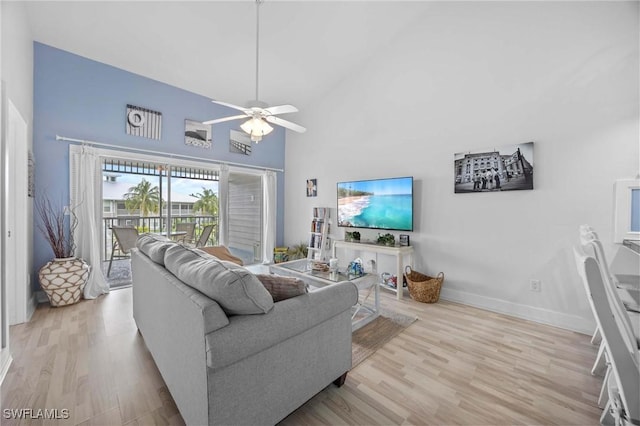living area with light wood-style flooring, ceiling fan, baseboards, and a high ceiling