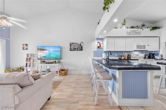kitchen featuring white appliances, a breakfast bar area, a sink, dark countertops, and high vaulted ceiling