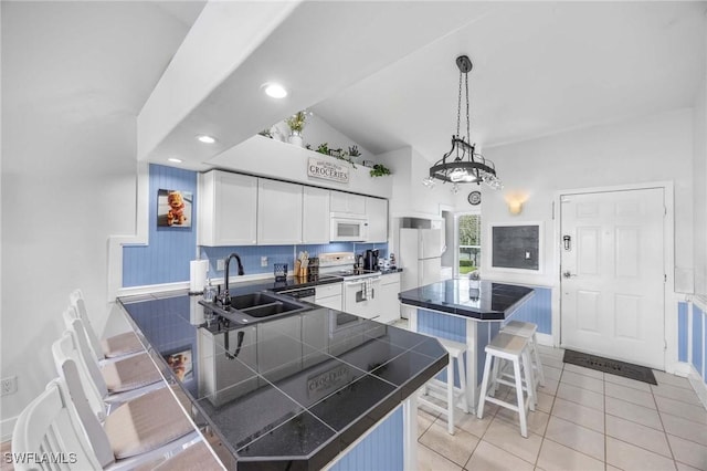 kitchen featuring white appliances, a sink, white cabinetry, light tile patterned flooring, and a kitchen bar