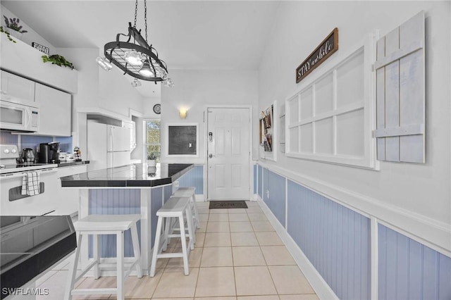 kitchen featuring white appliances, light tile patterned flooring, a kitchen breakfast bar, a center island, and white cabinetry