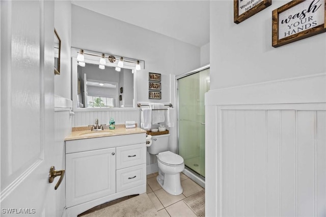 full bathroom with a stall shower, wainscoting, tile patterned floors, vanity, and toilet
