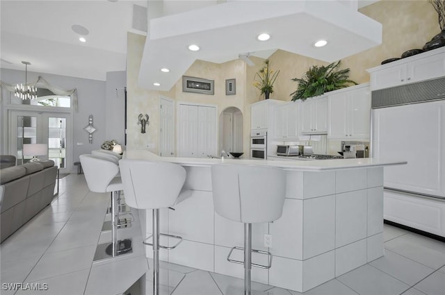 1428 SW 52nd Ln, Cape Coral, FL 33914 - kitchen featuring a breakfast bar area, white cabinets, a chandelier, paneled refrigerator, and light tile patterned floors