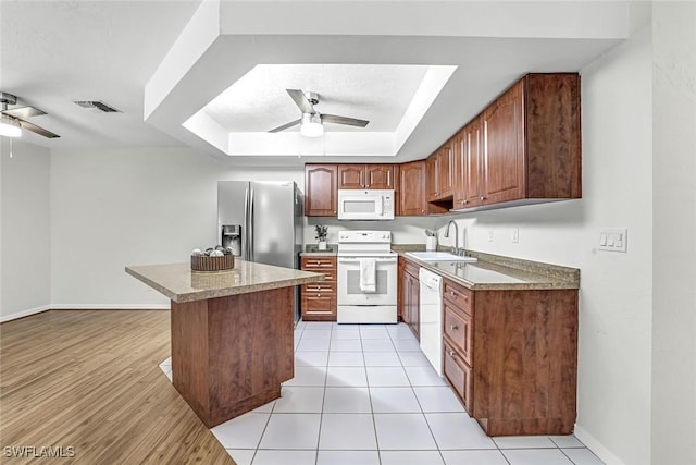 kitchen with white appliances, ceiling fan, a sink, a tray ceiling, and a kitchen island