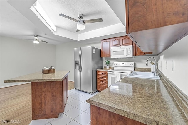 kitchen with white appliances, ceiling fan, a sink, a tray ceiling, and a textured ceiling