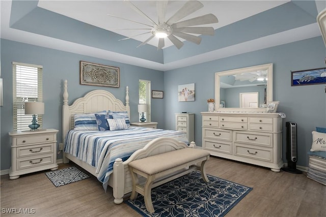 bedroom featuring a raised ceiling, wood finished floors, baseboards, and ceiling fan