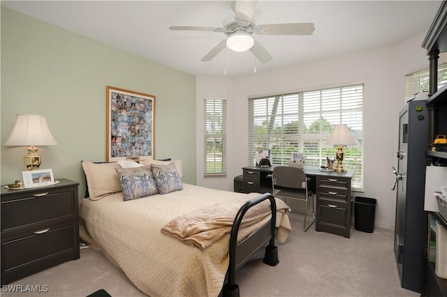 bedroom featuring light carpet, multiple windows, a ceiling fan, and a desk