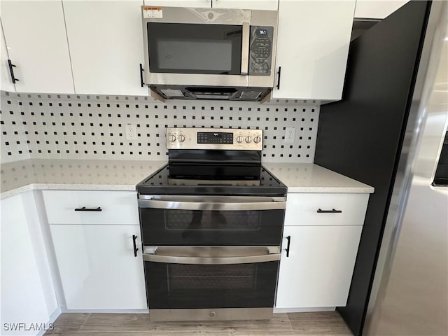 kitchen featuring stainless steel appliances, white cabinetry, light wood finished floors, and backsplash