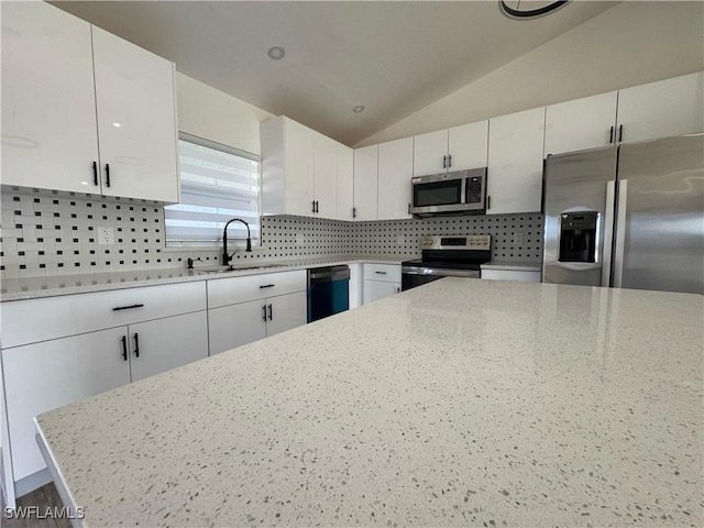 kitchen with appliances with stainless steel finishes, a sink, tasteful backsplash, white cabinetry, and lofted ceiling