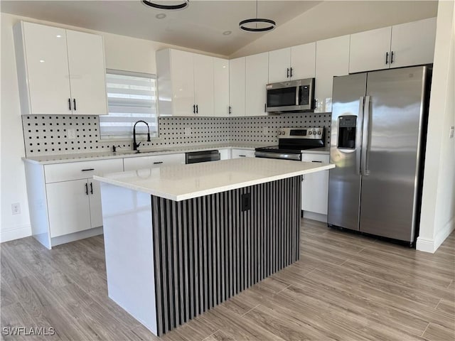 kitchen featuring appliances with stainless steel finishes, white cabinetry, light wood-style flooring, and lofted ceiling