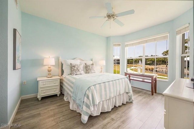 bedroom featuring multiple windows, wood finished floors, baseboards, and a ceiling fan