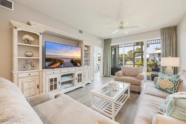 living room with a ceiling fan, light wood finished floors, and built in shelves