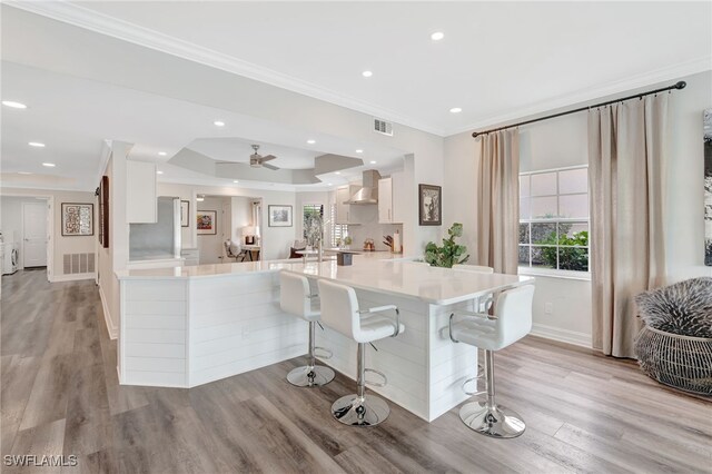 3580 Windjammer Cir Unit 1603, Naples, FL 34112 - kitchen with white cabinetry, crown molding, a breakfast bar, light countertops, and wall chimney range hood