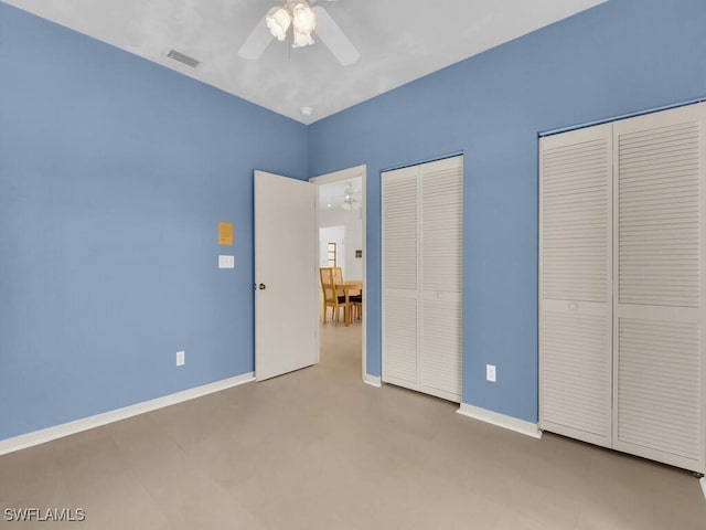 unfurnished bedroom with two closets, baseboards, and ceiling fan