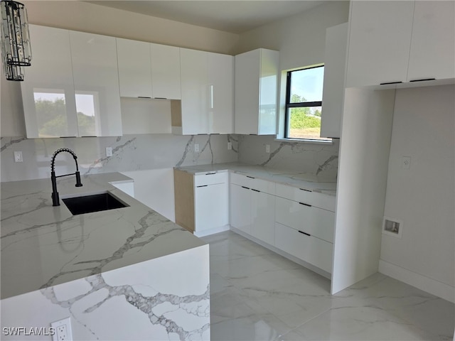 kitchen featuring a sink, modern cabinets, light stone countertops, tasteful backsplash, and white cabinets