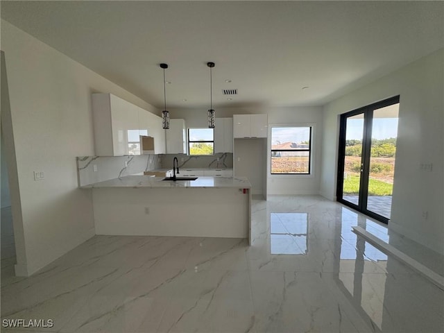 kitchen with a sink, light marble finish floors, white cabinets, baseboards, and a peninsula