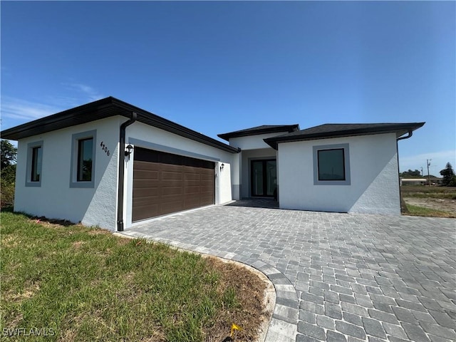 ranch-style home with stucco siding, an attached garage, and decorative driveway