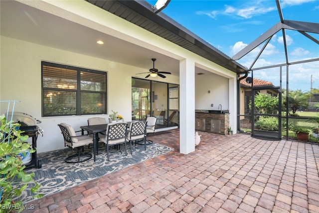 view of patio featuring an outdoor kitchen, ceiling fan, glass enclosure, outdoor dining area, and a sink