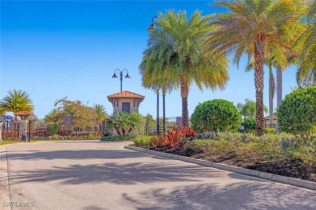 view of asphalt street with curbs, a gate, street lighting, and a gated entry