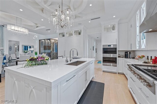 714 Killdeer Pl, Naples, FL 34108 - kitchen featuring a sink, wall chimney exhaust hood, a chandelier, light wood-style floors, and white cabinetry