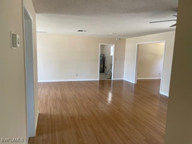 empty room with wood finished floors, water heater, baseboards, a textured ceiling, and ceiling fan