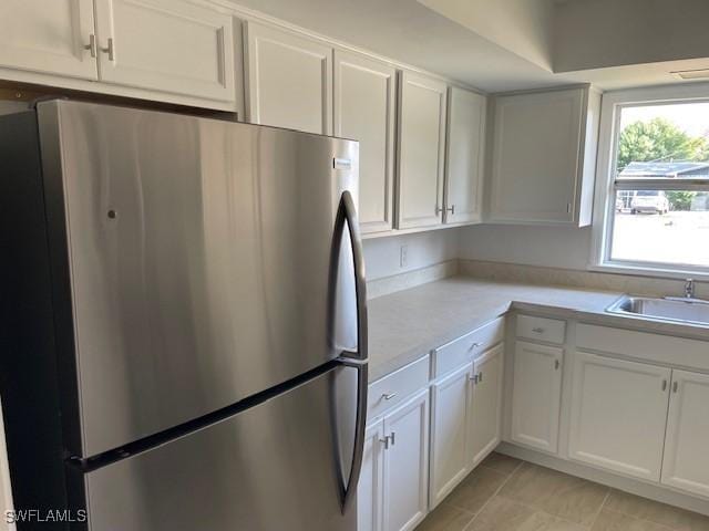 kitchen featuring freestanding refrigerator, a sink, light countertops, white cabinets, and light tile patterned floors