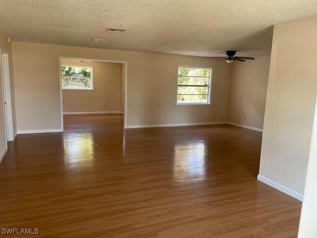 empty room featuring a textured ceiling, ceiling fan, wood finished floors, and baseboards