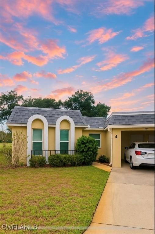 view of front of property with stucco siding, a lawn, a shingled roof, and concrete driveway