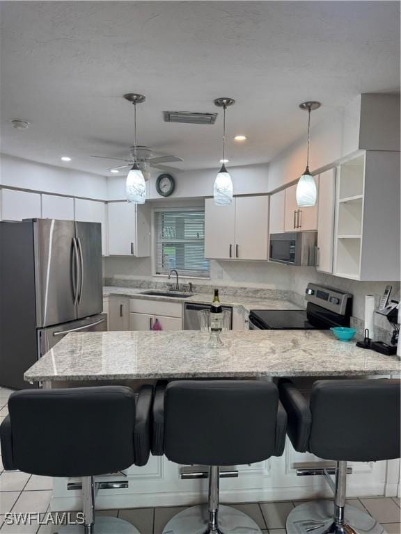 kitchen with stainless steel appliances, a peninsula, a sink, light stone countertops, and white cabinets