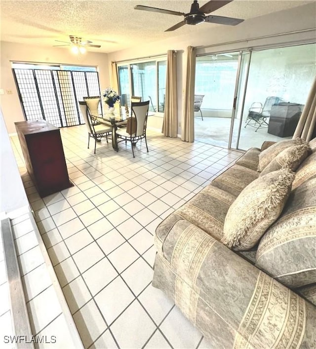 living room with a ceiling fan, a textured ceiling, plenty of natural light, and light tile patterned floors