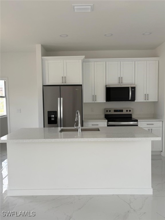 4118 4th St SW, Lehigh Acres, FL 33976 - kitchen with appliances with stainless steel finishes, light marble finish floors, a kitchen island with sink, white cabinets, and light countertops