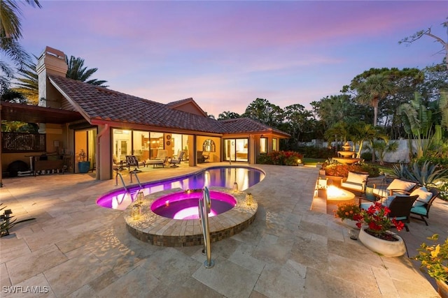 pool at dusk featuring a patio area, a pool with connected hot tub, and an outdoor living space with a fire pit